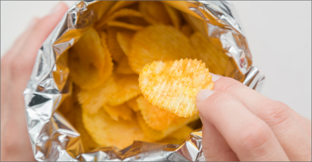 Close-up of a person’s hands taking potato chips from a foil snack bag.